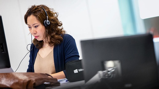 A person wearing a headset works at a laptop in an office setting.