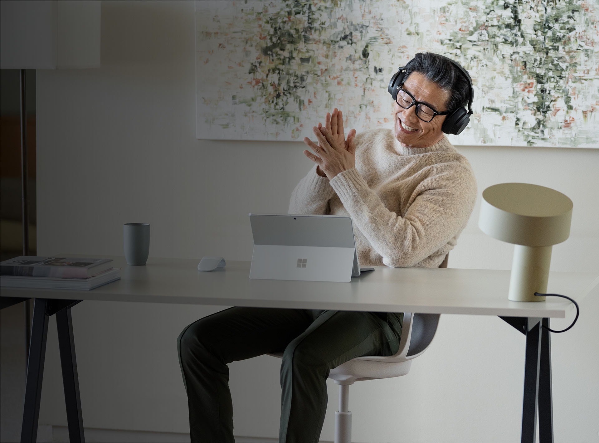 Een man zit in zijn thuiskantoor en geniet van zijn Surface Pro 9 met Surface Headphones 2+ op
