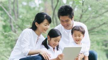 公園の木の下で一緒に ノート PC の画面を見ている家族