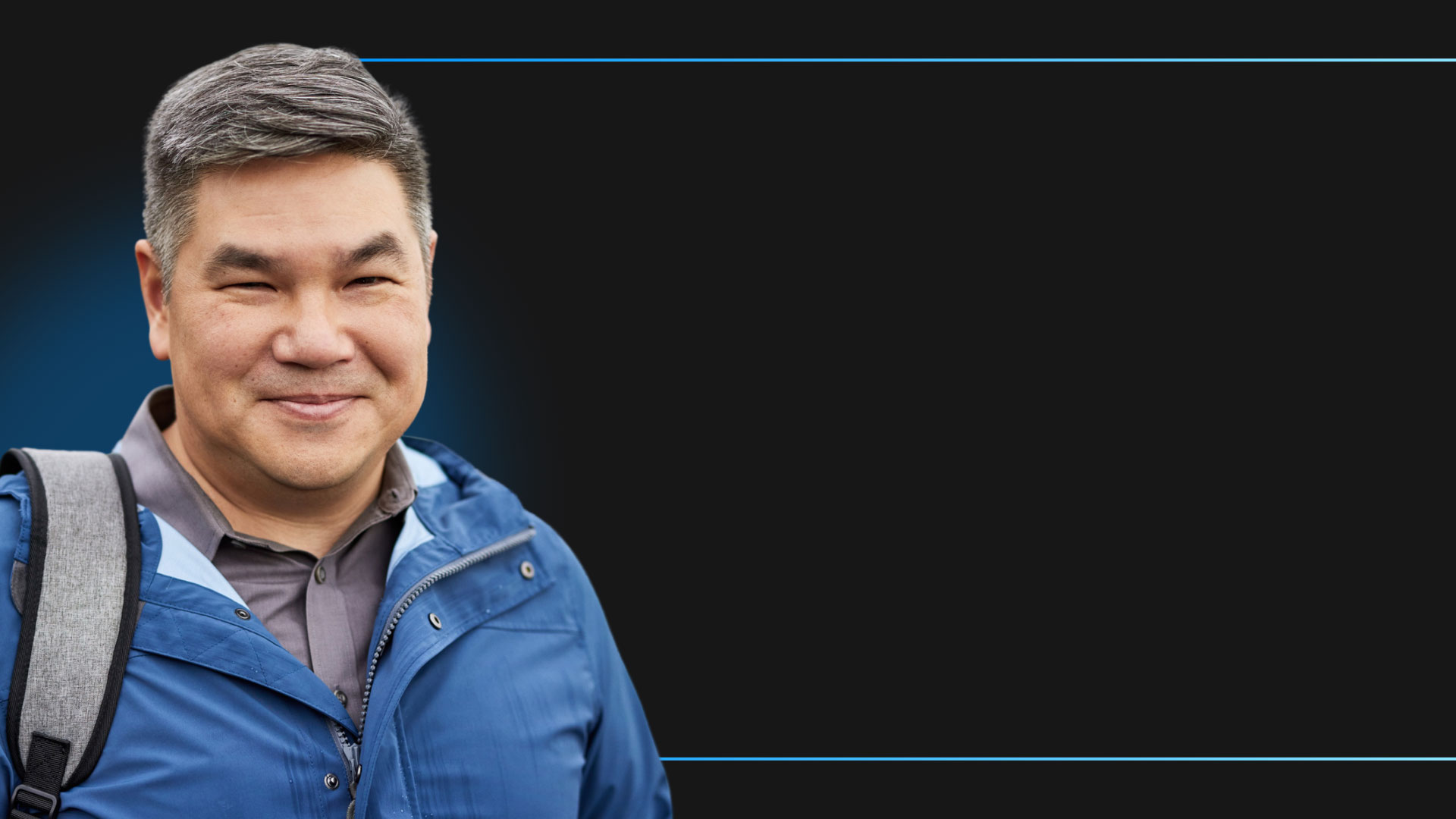 Kevin Cheung, Managing Director van PSC Noord-Amerika, kijkt glimlachend naar de camera terwijl hij een regenjas, rugzak en overhemd draagt