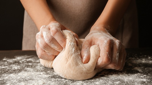 Two hands kneading dough covered in flour.