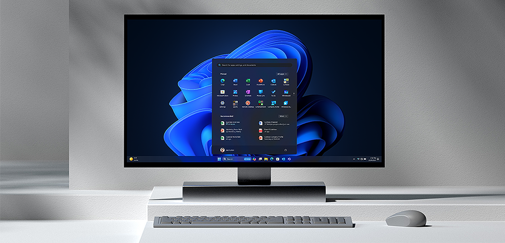 An all-in-one device with monitor displaying the Windows 11 start screen, keyboard and mouse
