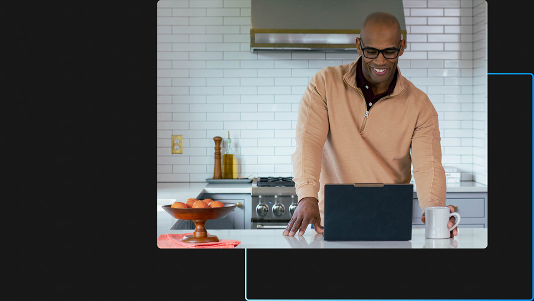 Een persoon in een keuken die op zijn of haar laptop werkt terwijl hij of zij lacht en een mok vasthoudt