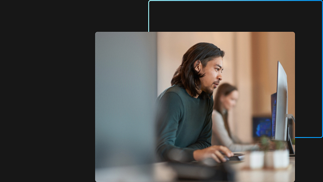 Una persona en primer plano y una persona en segundo plano trabajando en sus computadoras en una oficina con una Licencia Windows 11 Pro