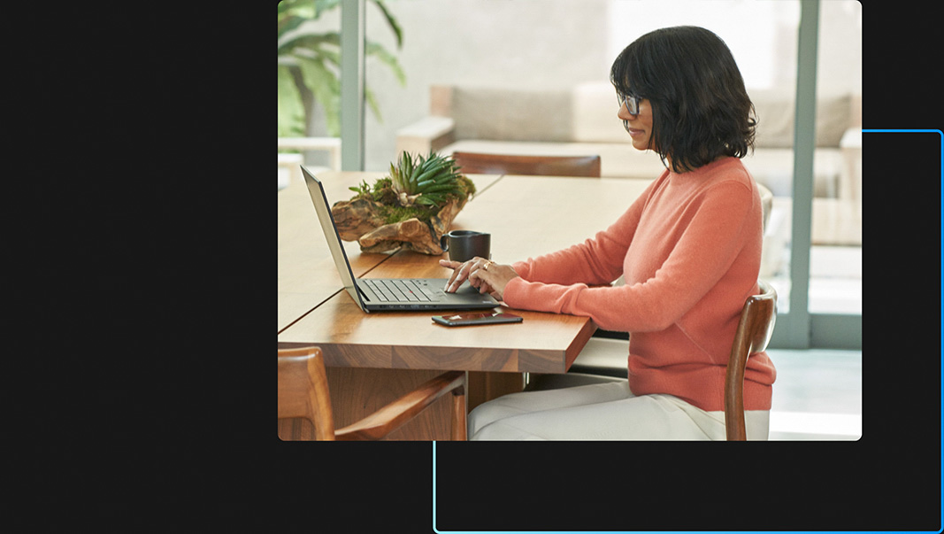 Une personne assise à une table travaille sur son ordinateur portable avec son appareil mobile posé à côté d’elle.