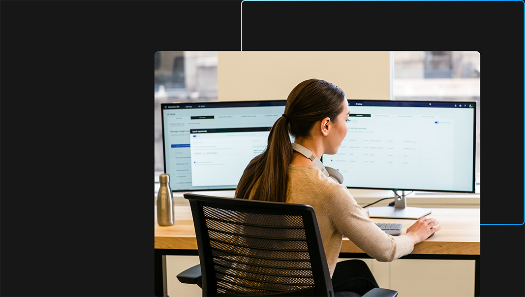 Een persoon in een kantoor die werkt op zijn of haar laptop en twee monitors en een muis