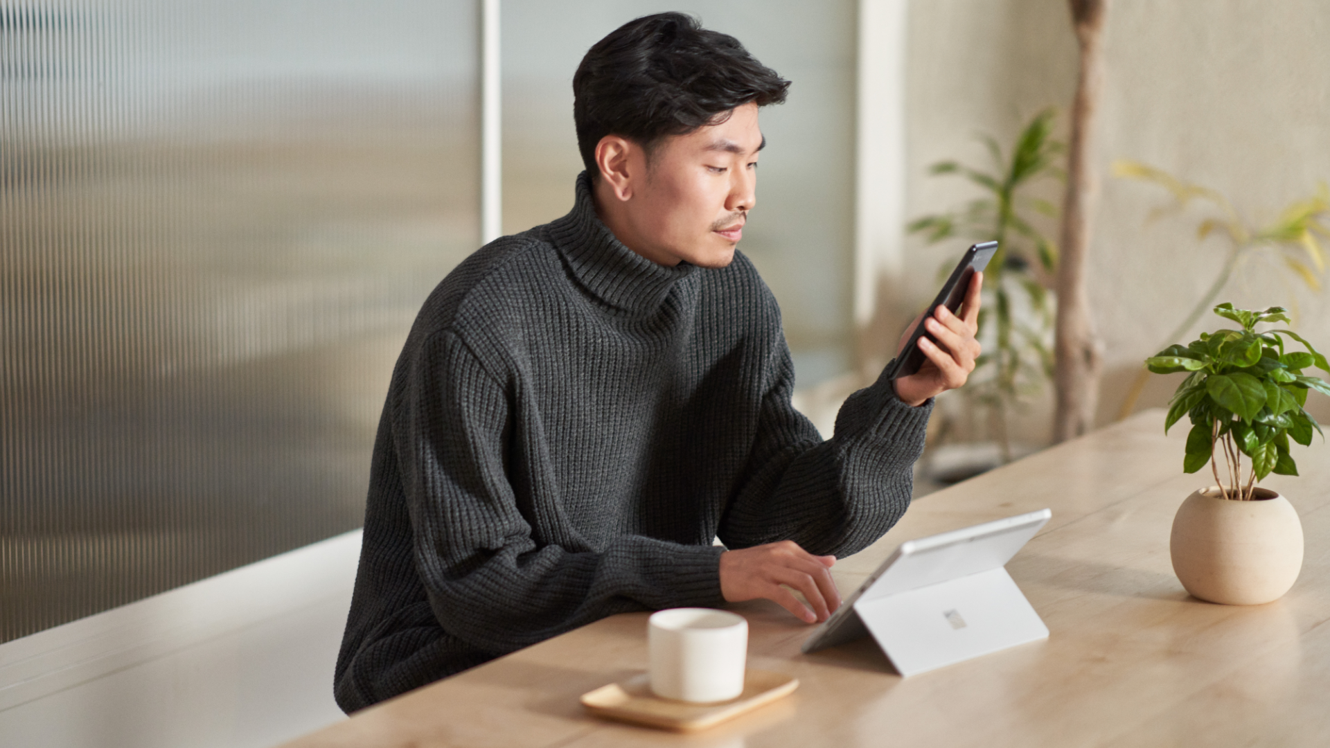 A person sitting at a kitchen island with a Surface tablet looking at a mobile phone.