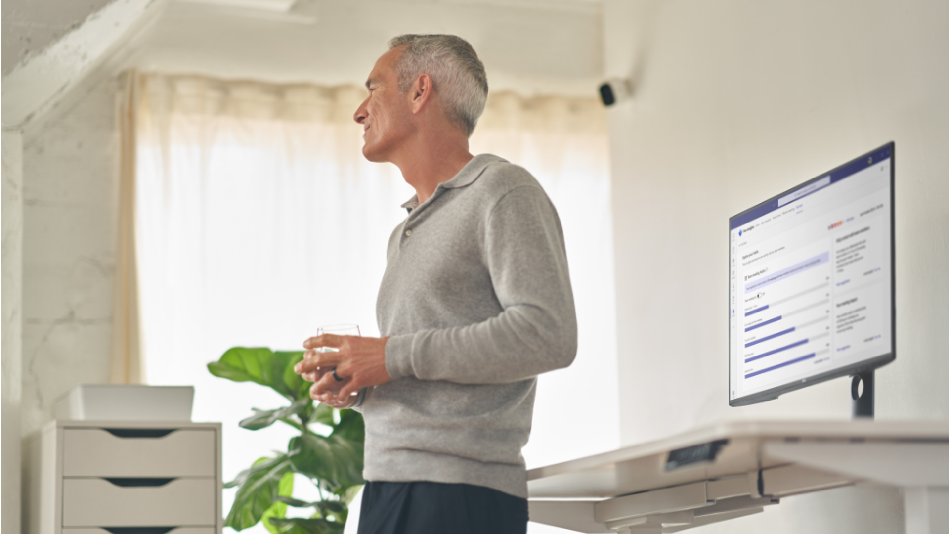 A person standing in front of their desk looking towards the window behind them.