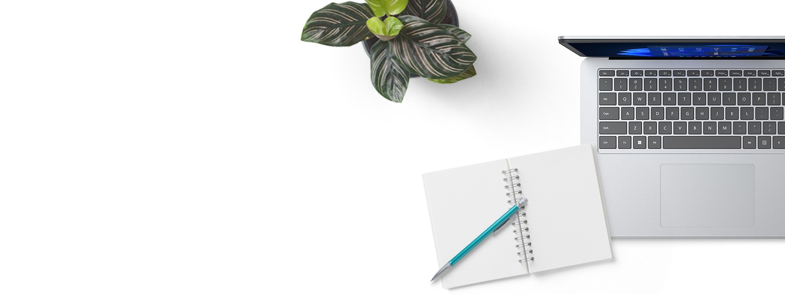 A Surface device is seen with a plant and a notepad and pen nearby
