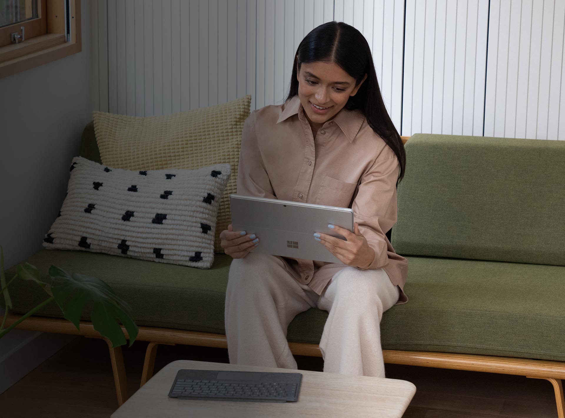 Žena sedící doma na gauči a spokojeně používá Surface Pro 9