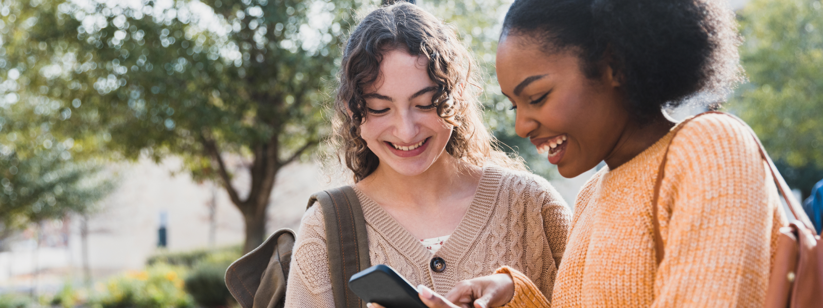 Two adolescent girls smile while gazing at a cell phone.