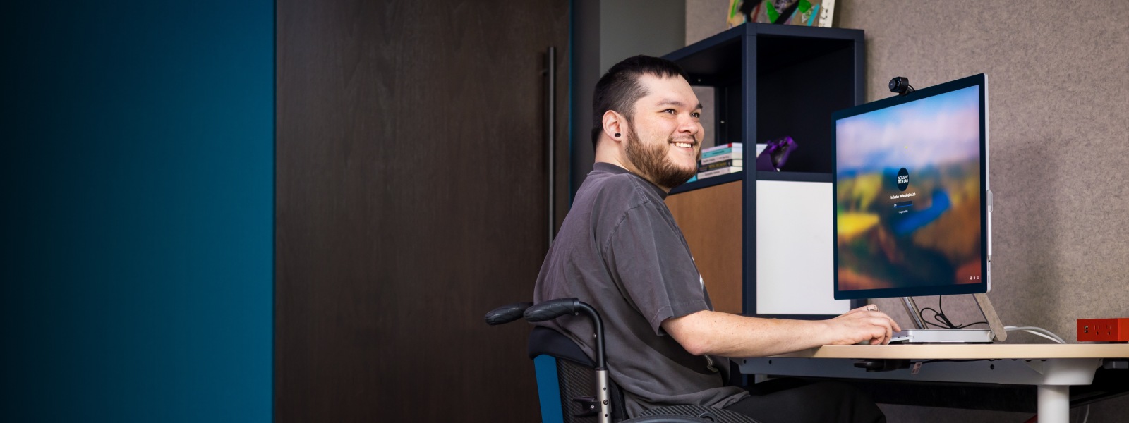 Una persona sonriente en una silla de ruedas trabaja con su escritorio.