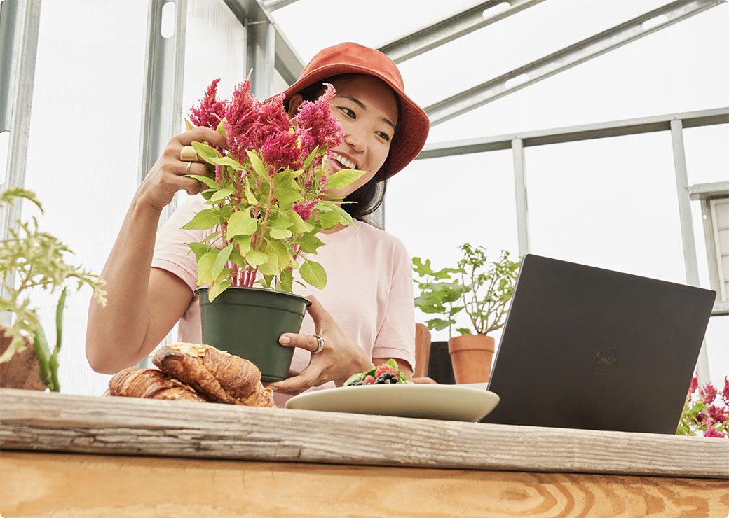 Eine Frau hantiert mit einer Pflanze und schaut auf einen Laptop