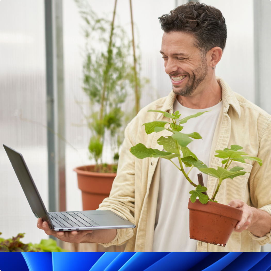 片手で PC を持ち、もう片方の手で植物を持っている笑顔の男性