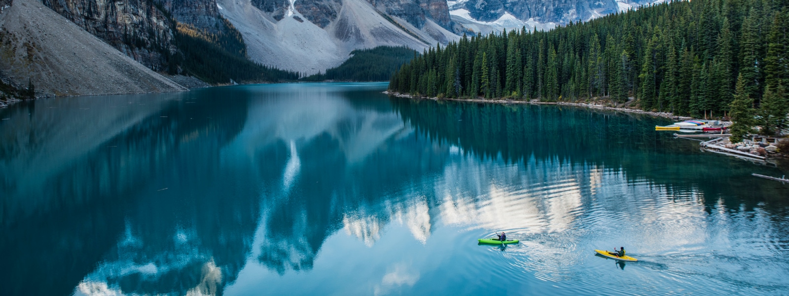 Two individuals kayaking across a lake in the middle of snowy mountains.