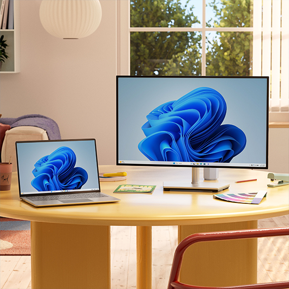Portátil y equipo de escritorio, sobre una mesa, con la flor de Windows en la pantalla.