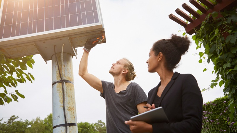 Low angle view of a garden architect adjusting a solar panel with a colleague holding a tablet computer.