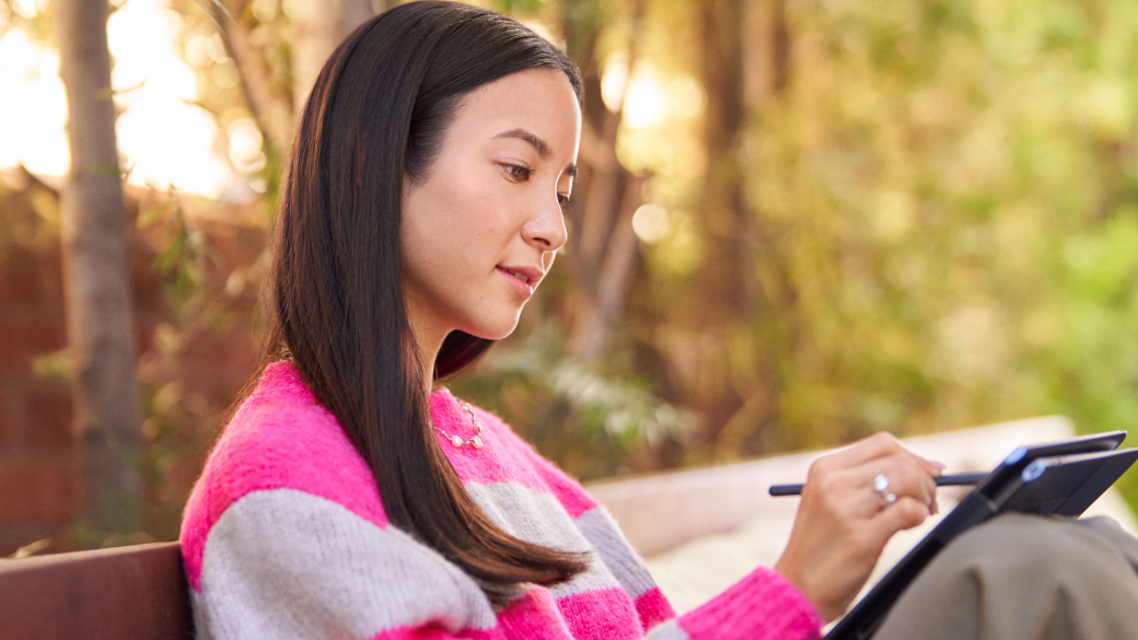 Moteris sėdi ant parke ant suoliuko ir kompiuteryje naudoja skaitmeninį liestuką