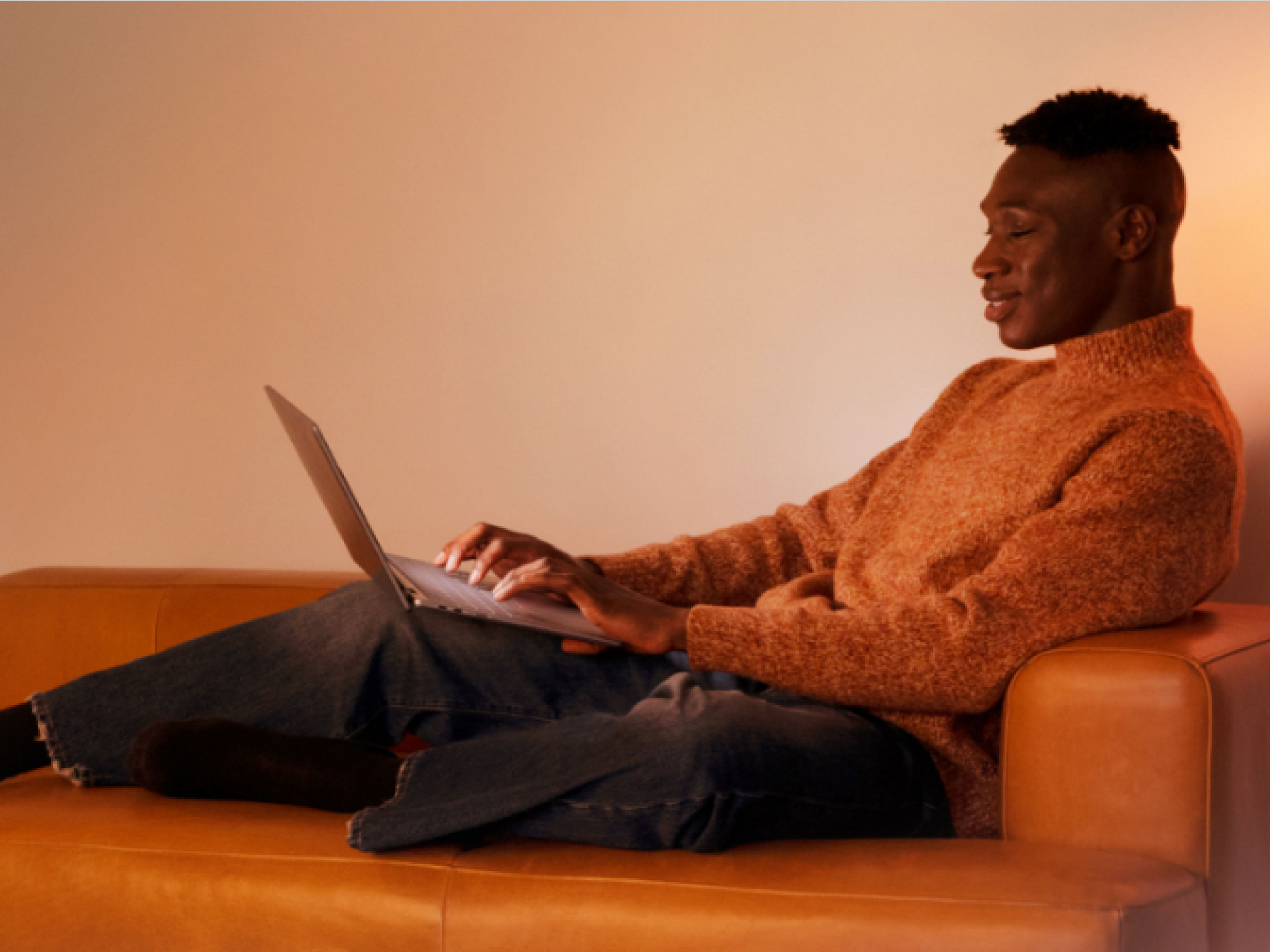 オレンジ色のソファでくつろいで、ノート PC を使用する男性