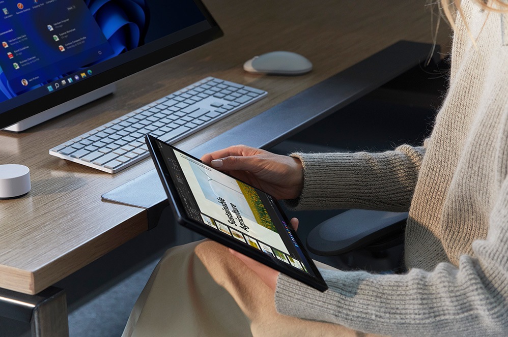 A person holds their Surface device in their hands while seated at a desk