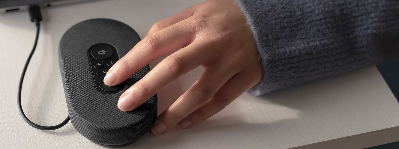 A hand lays on a Microsoft Modern USB-C Speaker that is plugged into a laptop port