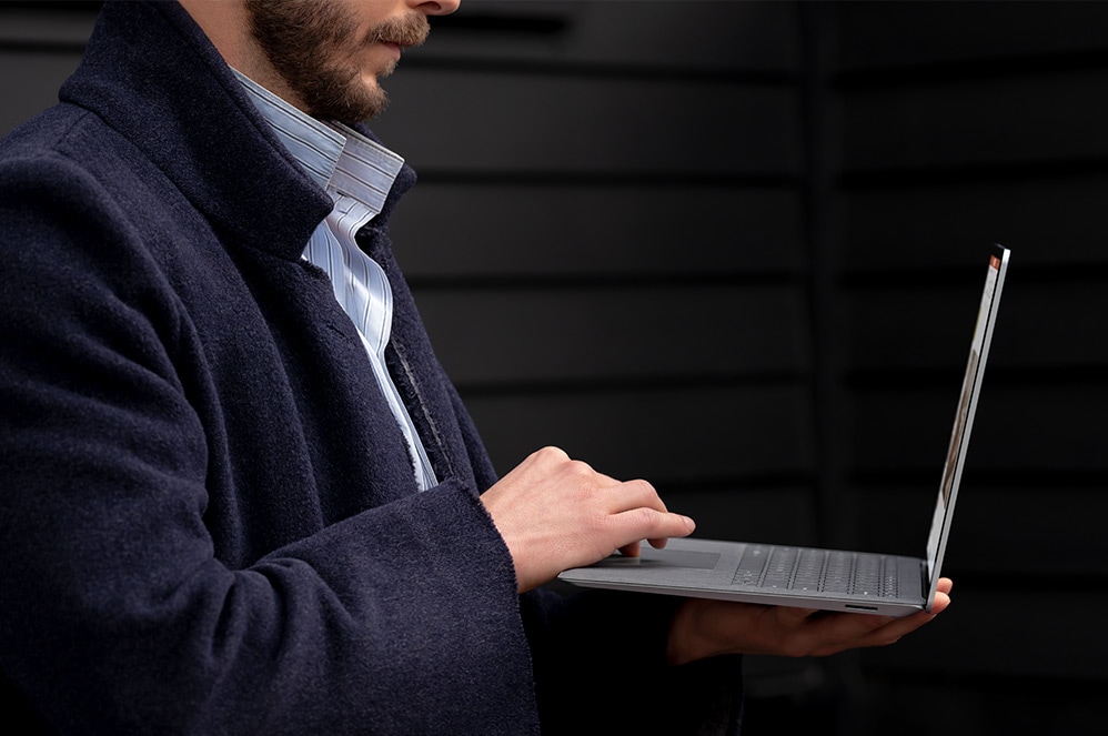 A person holds their Surface device to their chest while interacting with the trackpad