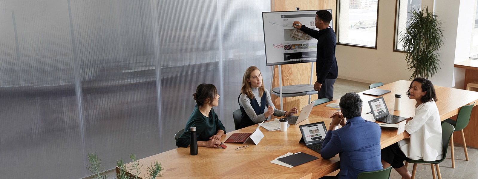 モダンな会議室で Surface Laptop を使い共同作業を行っている同僚たち。