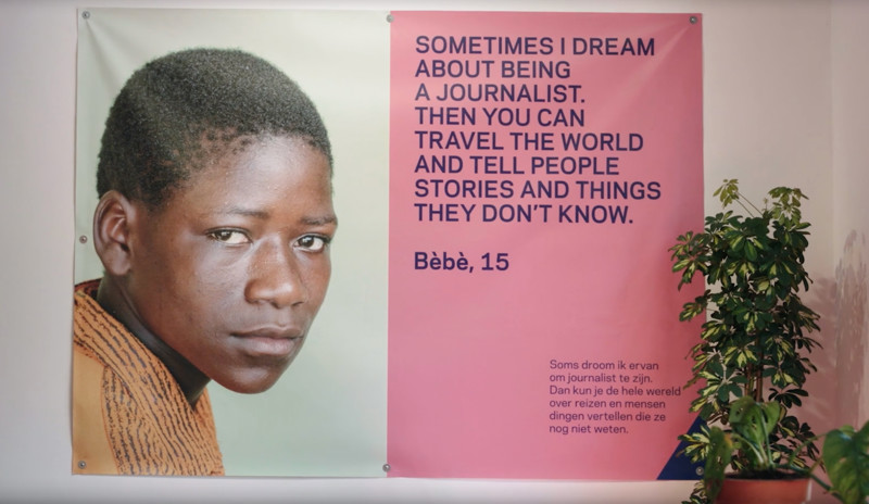 A wall tapestry with an image of a child named Bèbè and a quote from them talking about their dream of being a journalist.