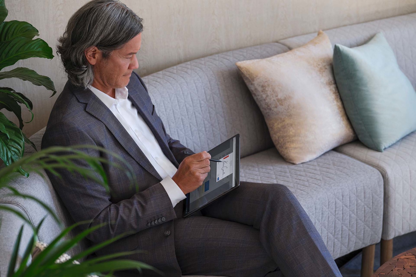 一个坐在办公室大厅沙发上的人，使用 Surface 超薄触控笔 2 在 Surface Pro 8 上书写