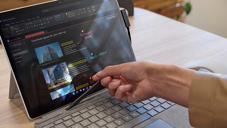 A person's hand is observed placing Surface Slim Pen 2 into the built-in storage inside Surface Pro Signature Keyboard
