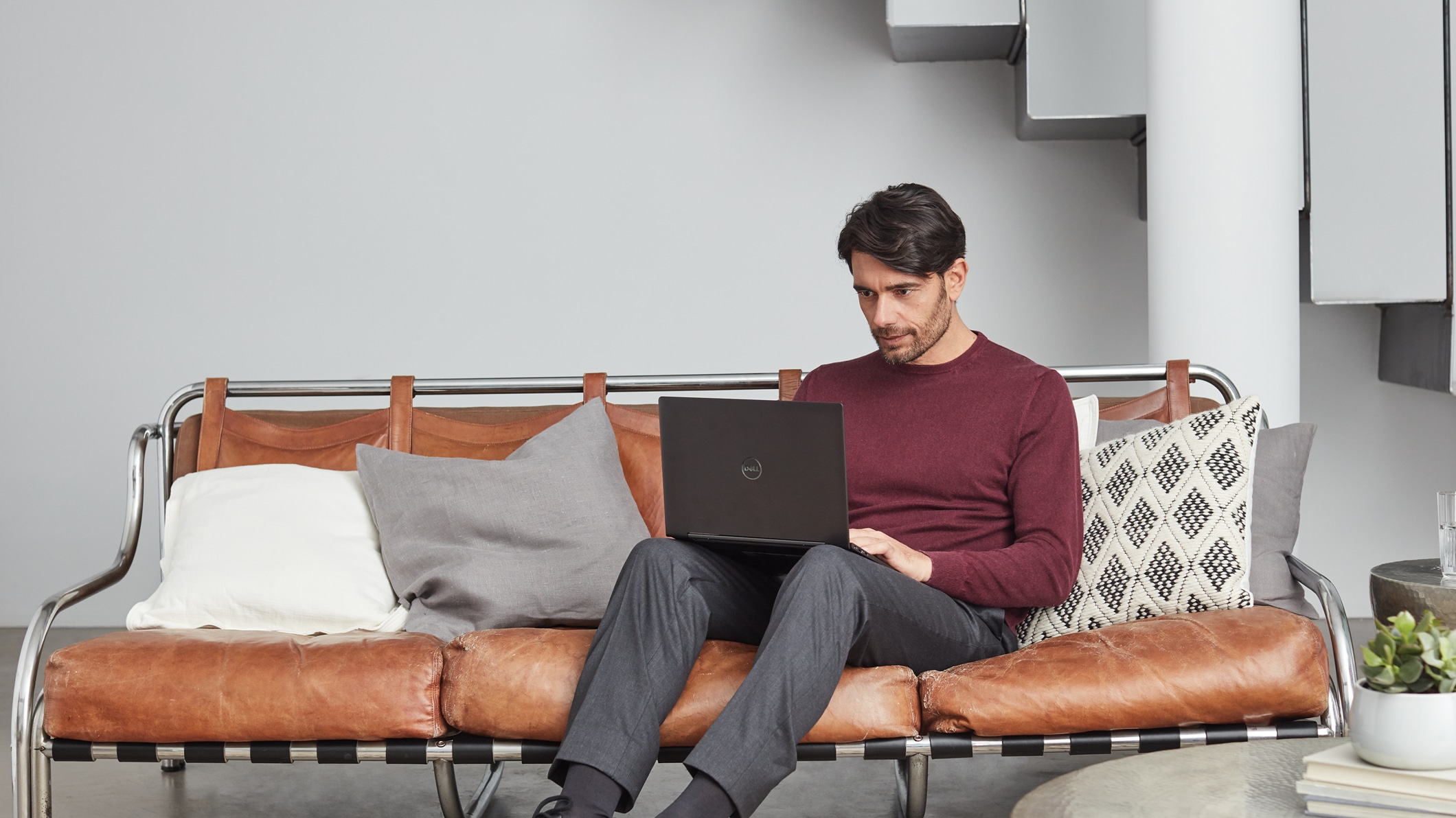 Um homem usa seu laptop sentado em um sofá em casa.