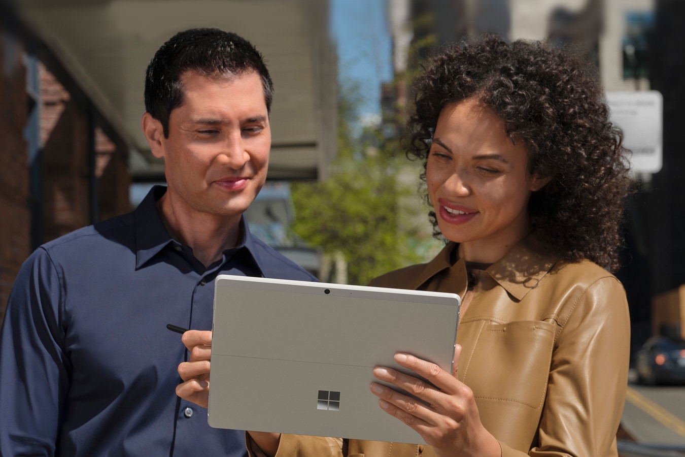 Two people stand outside on the pavement in a metropolitan city viewing the screen of their Surface Pro X in Tablet Mode