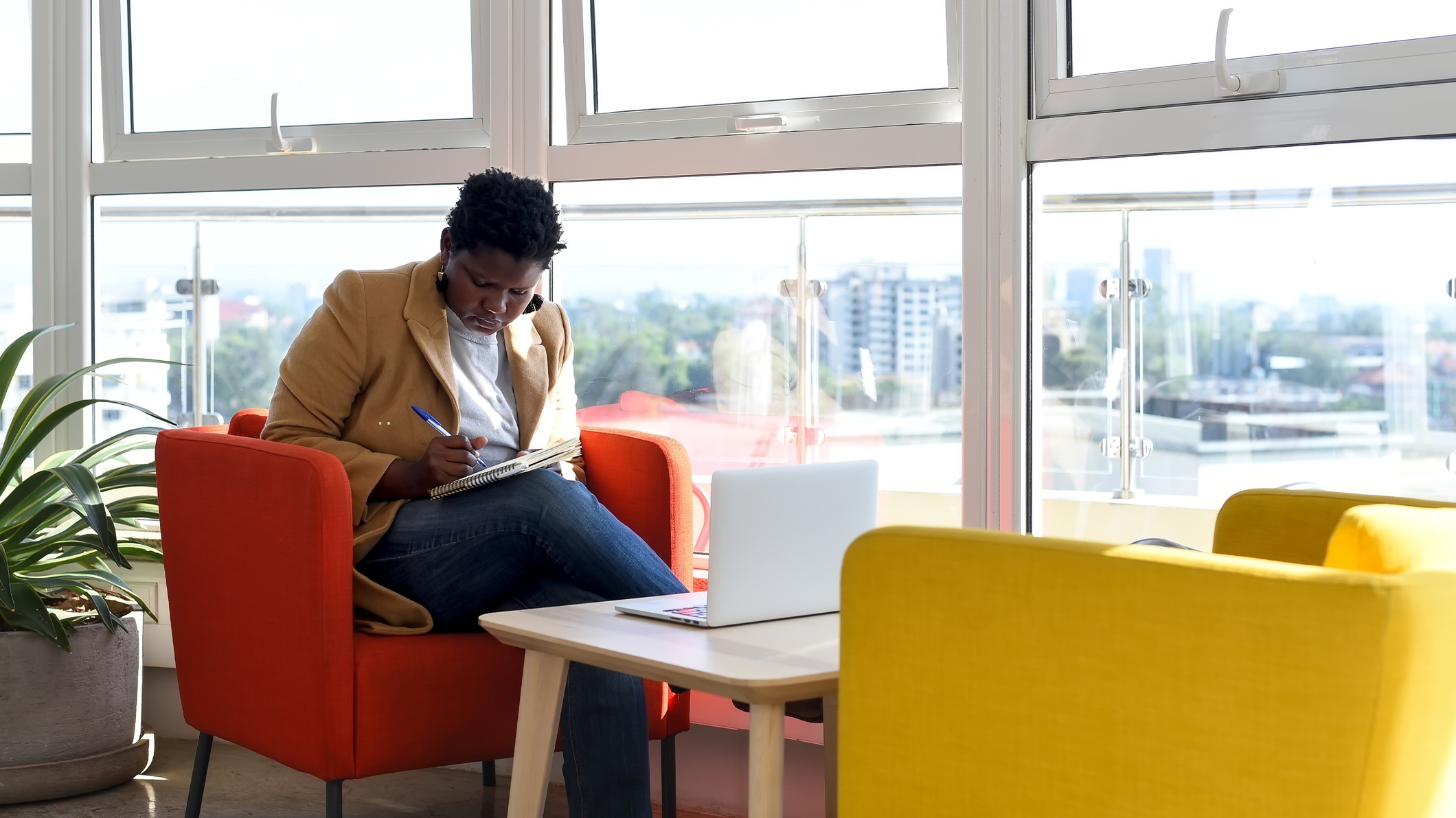 Una mujer toma notas sentada con su equipo portátil en una oficina moderna.