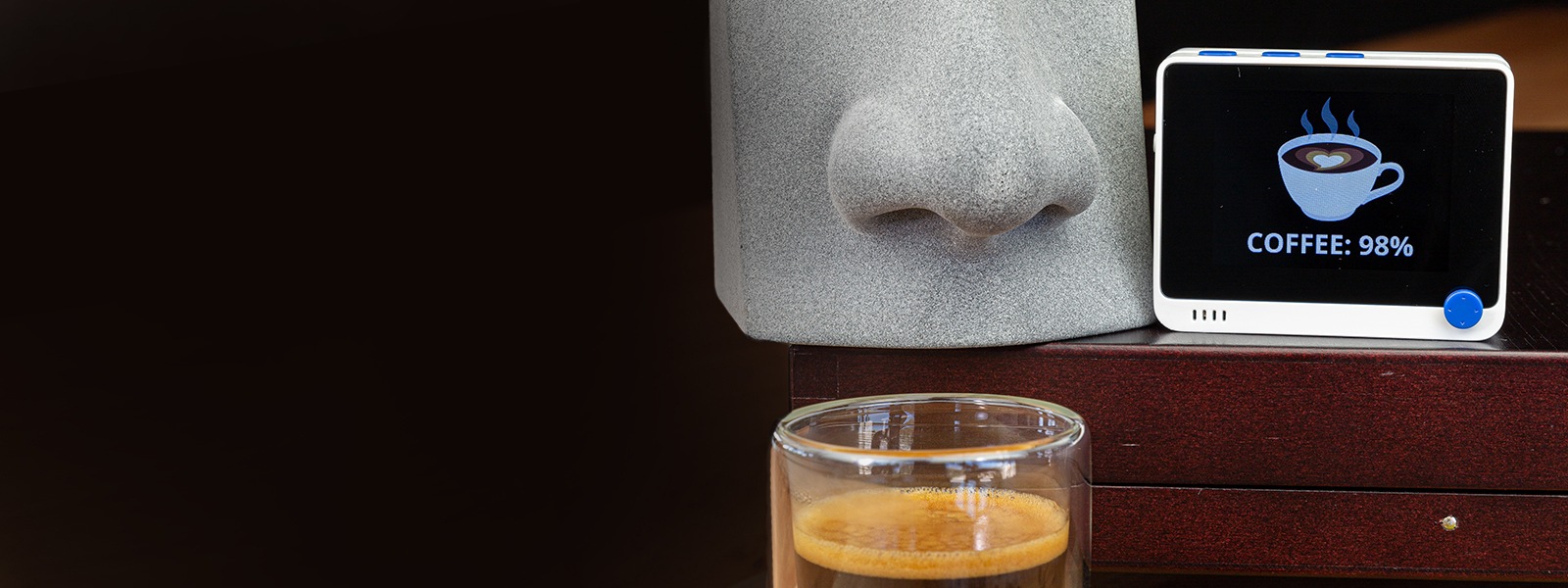 A representation of a human nose smelling a cup of coffee with a device showing the item is 98% coffee.