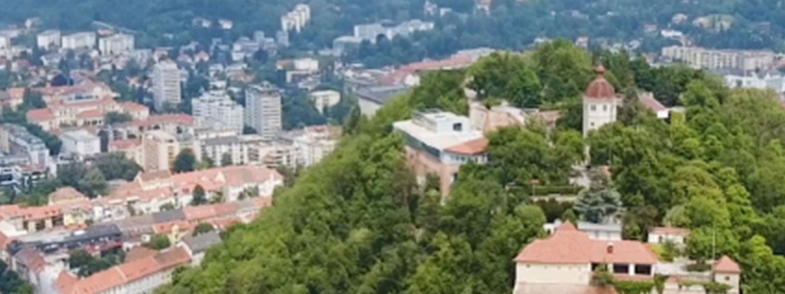 Bild zeigt eine Stadt von oben, auf dem ein Hügel voll mit Bäumen im Fokus steht.