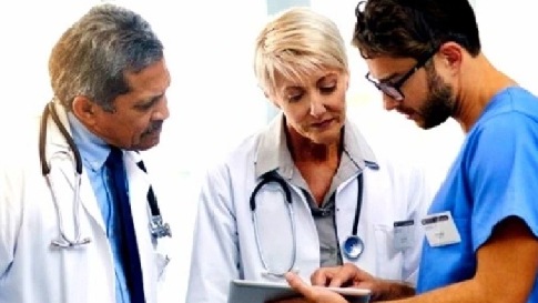 Drei Ärzte stehen nebeneinander. Einer zeigt den beiden anderen etwas am Tablet.