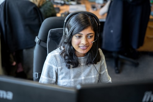 A woman sitting at a desk behind a monitor wearing a headset. She appears to be on a Business Voice call.