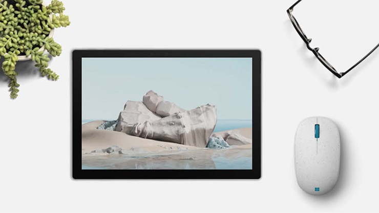 Máy tính bảng với màn hình có hình ảnh đại dương, bên cạnh chiếc Microsoft Ocean Plastic Mouse và một cặp kính đọc sách