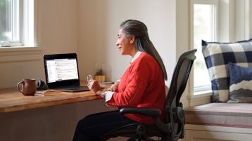 Henkilö istumassa työpöydän ääressä ja käyttämässä kannettavaa tietokonetta.