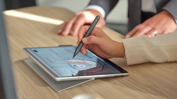 기업용 Surface Pro 8의 화면을 향해 Surface 펜을 들고 있는 사람의 손.
