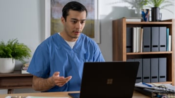 A nurse wearing scrubs using a laptop.