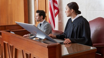 Um juiz e um colega sentados em suas mesas à frente de um computador grande.