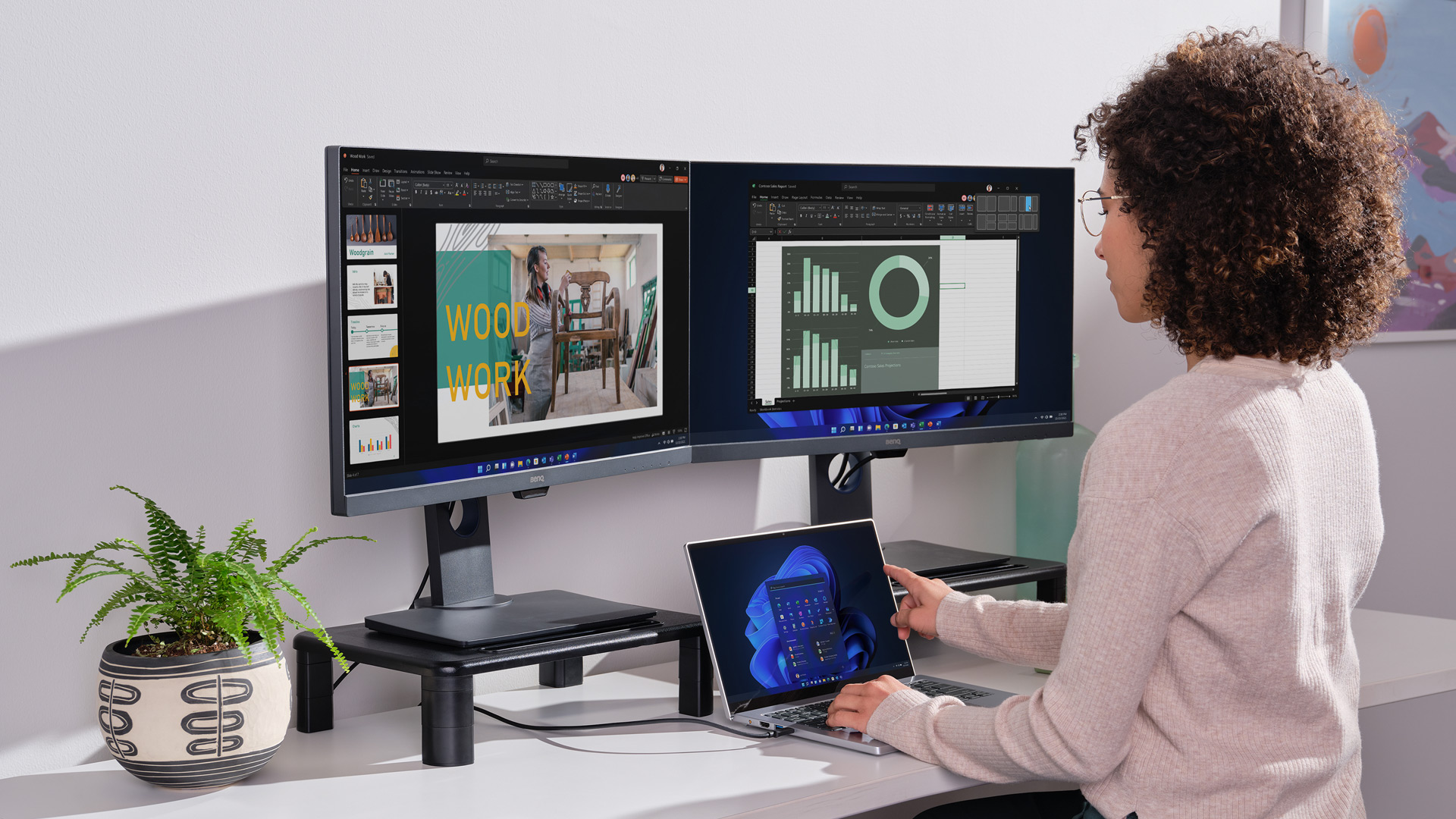 Een vrouw met bril op een werkstation met twee beeldschermen en een laptop waarop verschillende functies van Windows 11 worden weergegeven
