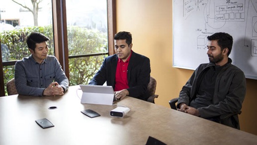 Three men sitting in an office looking at a computer.