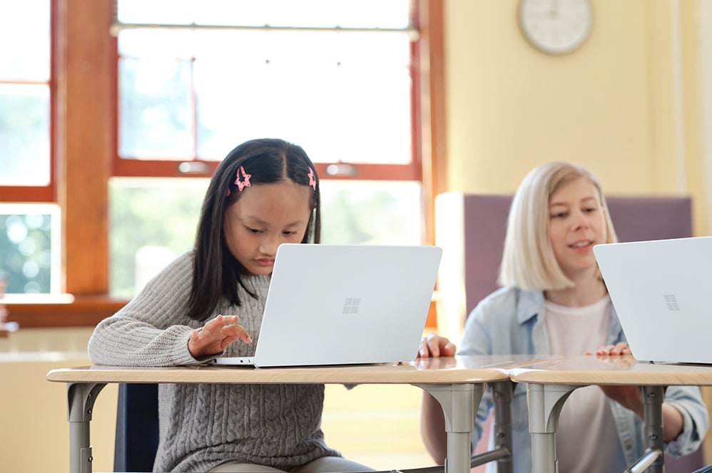 教室のカーペットの上で Surface Laptop SE を使用する子ども。