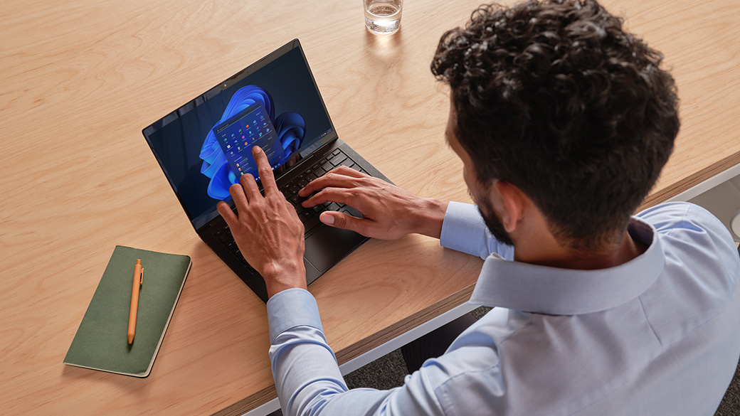 A man using a laptop that is displaying the Windows 11 start screen