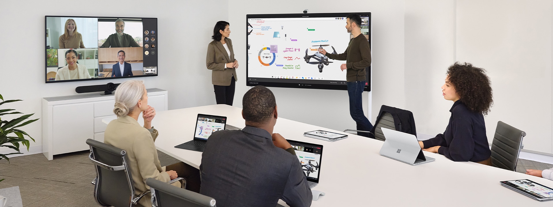 Dos trabajadores colaboran mediante Surface Hub 2S mientras lideran una reunión virtual en Teams en un dispositivo Surface Laptop sobre un escritorio cercano