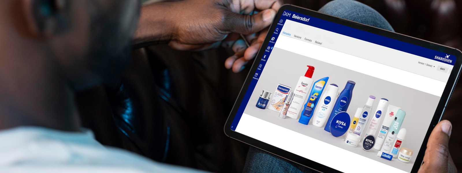 Das Bild zeigt einem Mann, der ein Tablet hält auf dem Beiersdorf Produkte zu sehen sind.