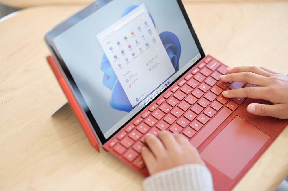 两只手在波比红颜色的 Surface 专业键盘盖上打字