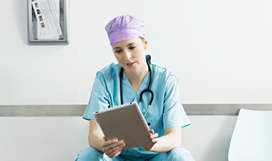 A medical professional in scrubs with a stethoscope around their neck looking at a tablet.
